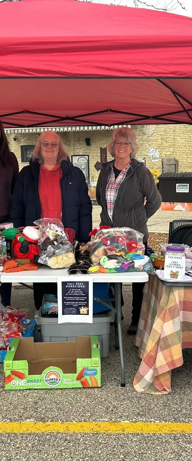 Volunteers at a Fall Fest collection table beside a Fort Atkinson Food Pantry donation barrel