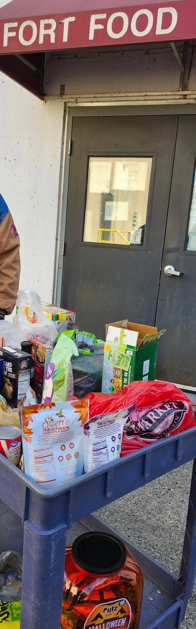 A volunteer with a cart of donated groceries under the Fort Food Pantry awning