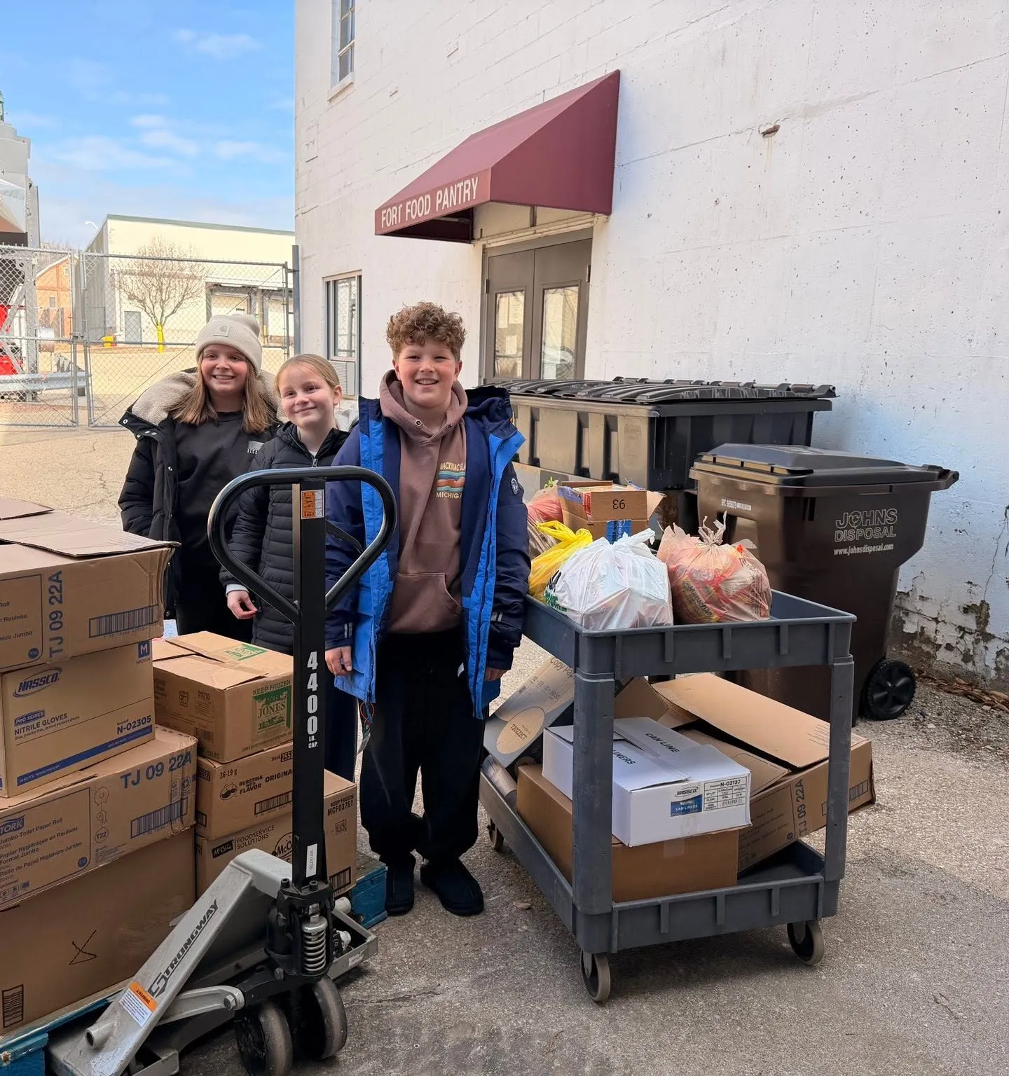 Three young volunteers with a loaded cart outside the Fort Atkinson Food Pantry door