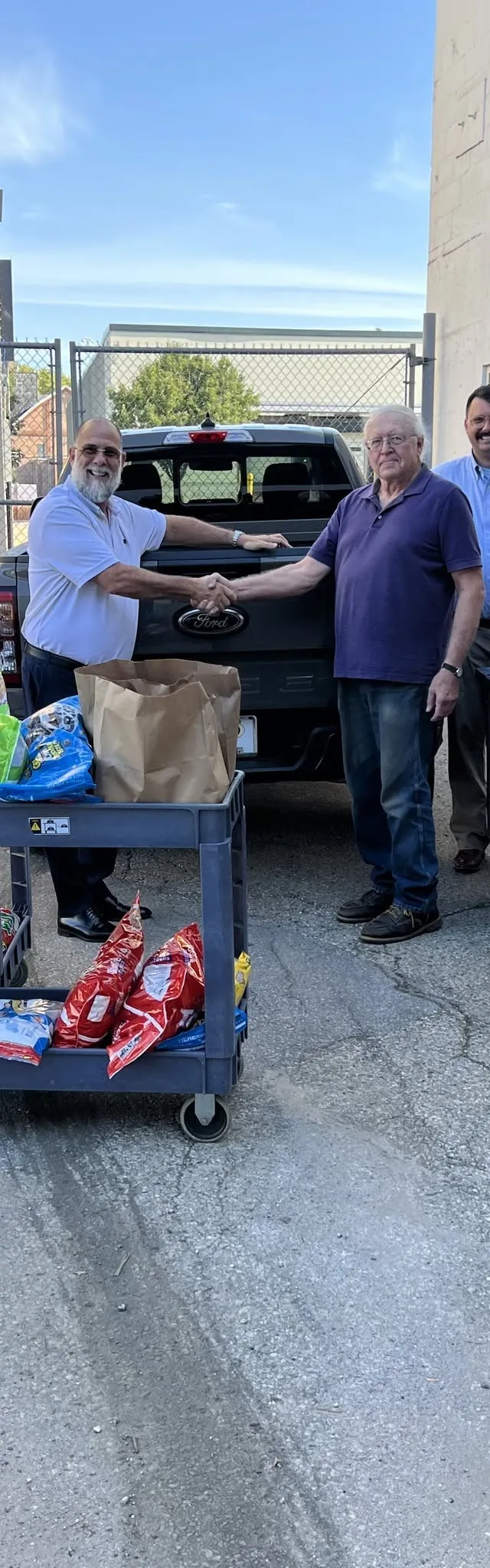 Four people shaking hands beside carts of donated food at the pantry's back door