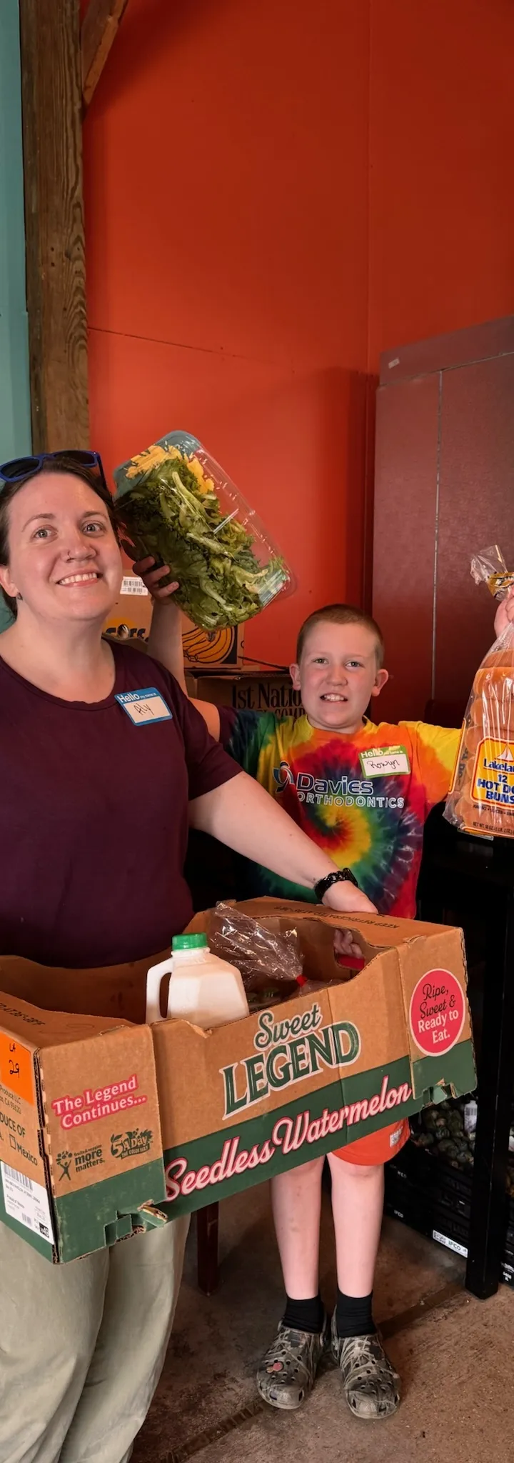 A Sunrise Reach volunteer and a young helper carrying a box of groceries at the monthly pantry