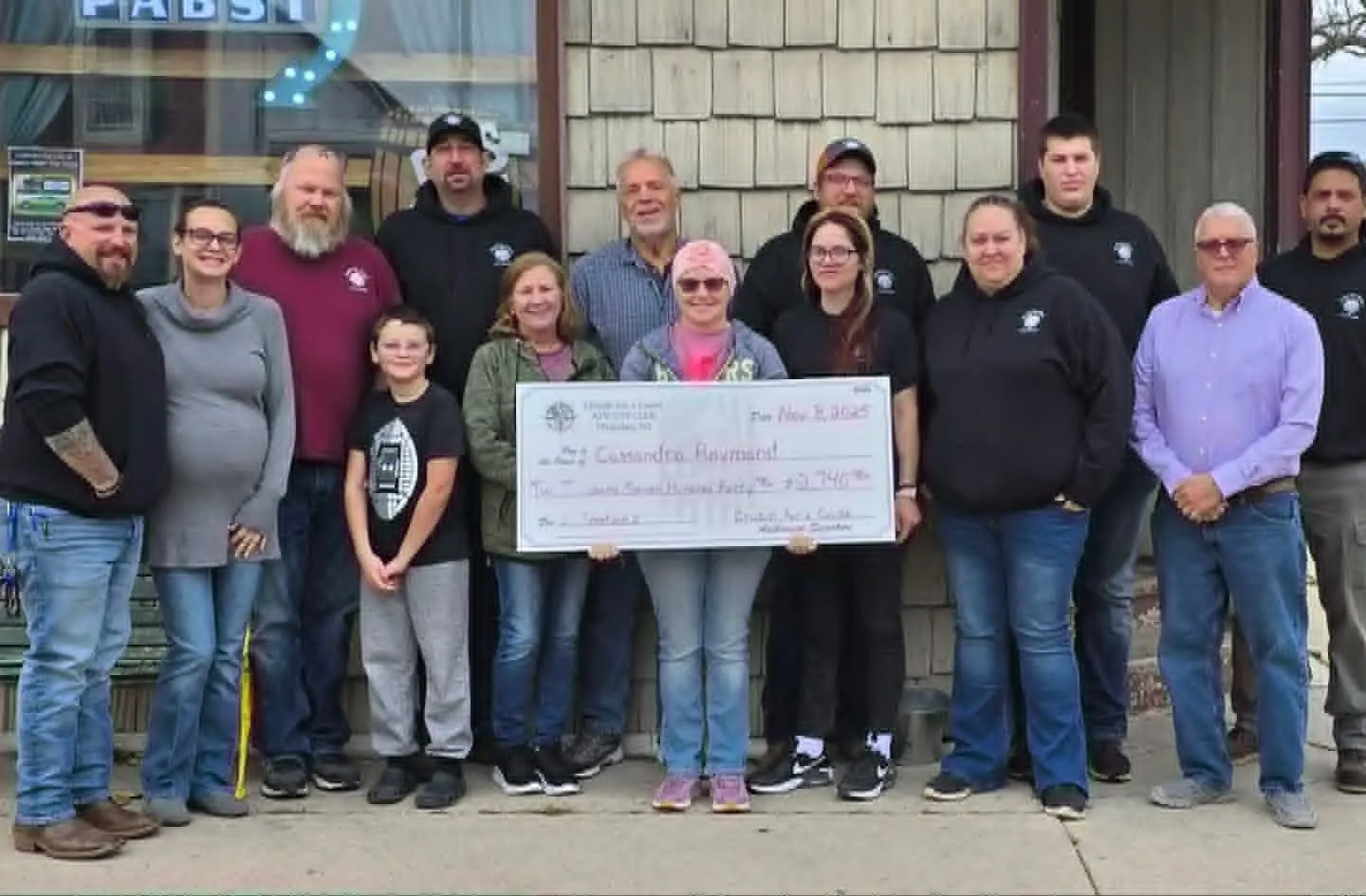 Cruzin' for a Cause members presenting a donation cheque to a family outside a Waterloo bar