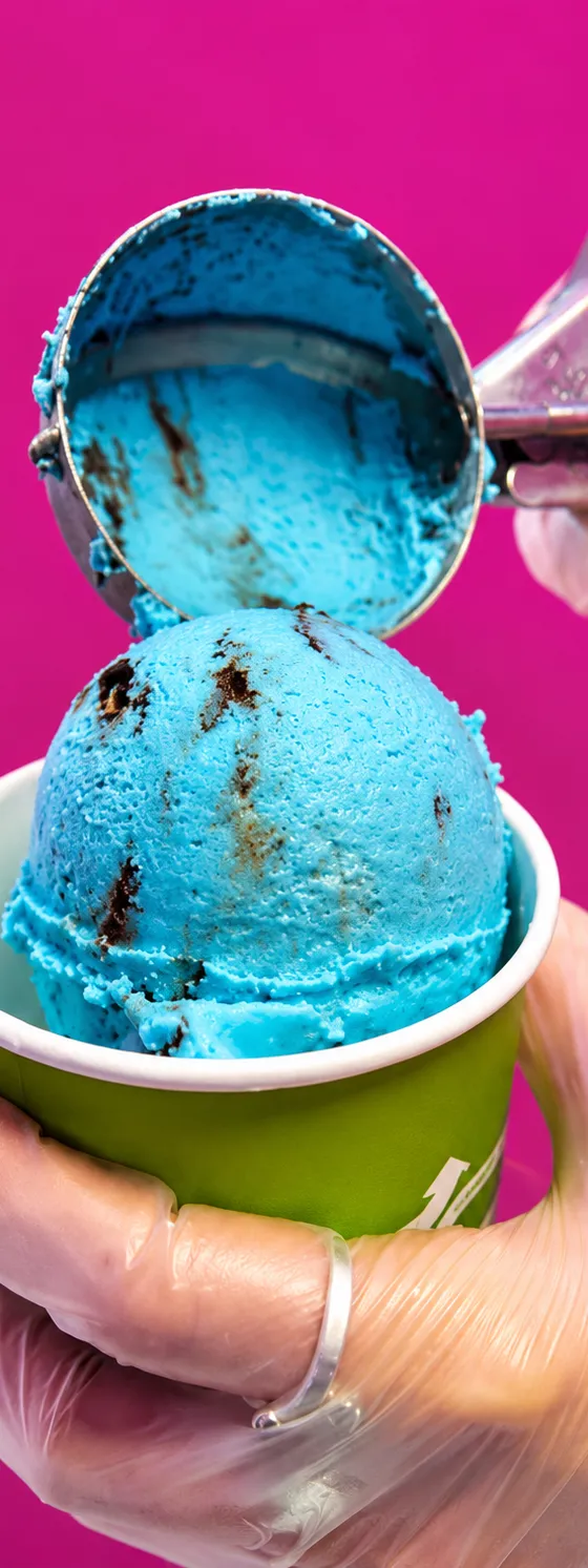 A gloved hand scooping bright blue ice cream into a cup