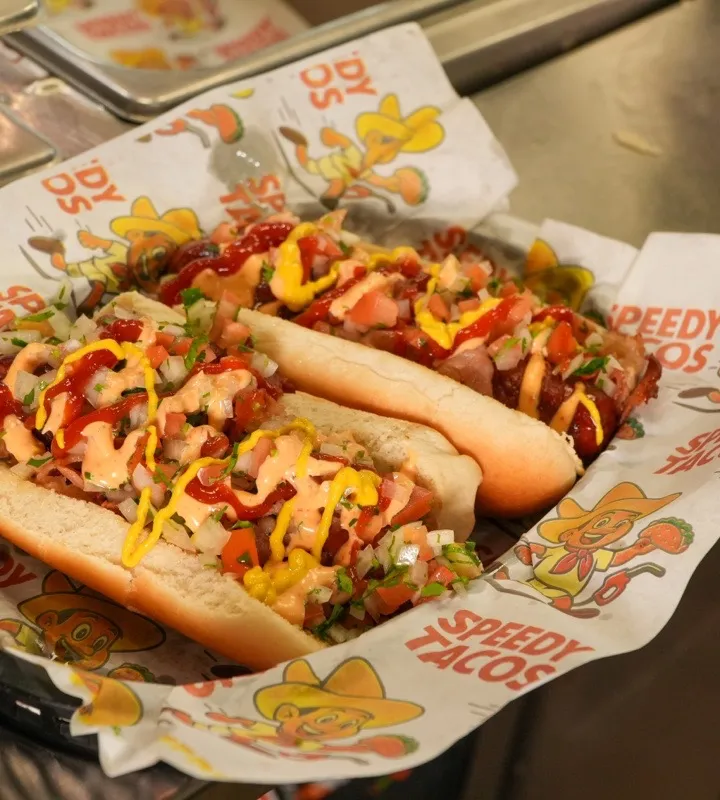 Two hot dogs topped with pico de gallo, ketchup, and mustard in a Speedy Tacos basket