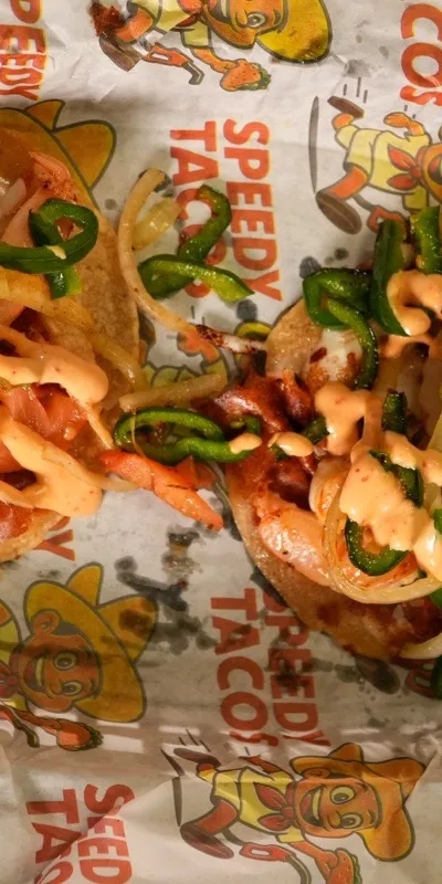 Two crispy shrimp tacos on Speedy Tacos paper with jalapeno and a chili crema drizzle