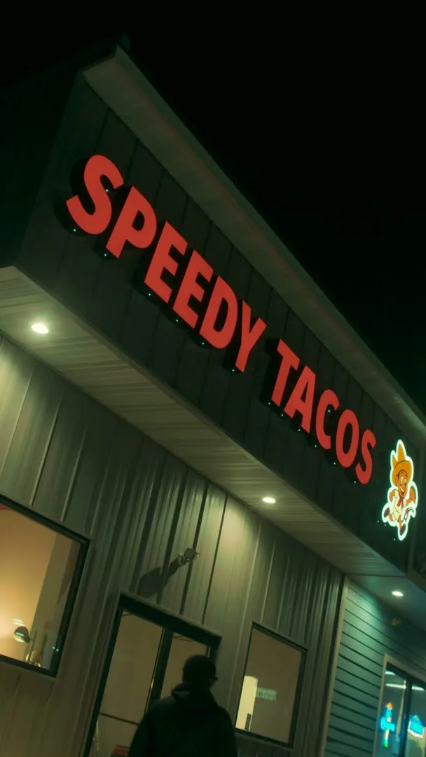 The lit Speedy Tacos sign on the corner of the store at night